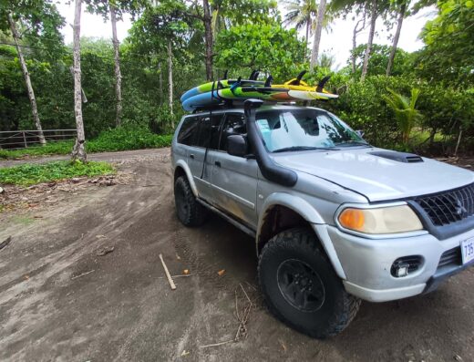 Silver SUV equipped with surfboards on roof rack, parked in lush tropical setting, ready for Soul Tours transportation services.