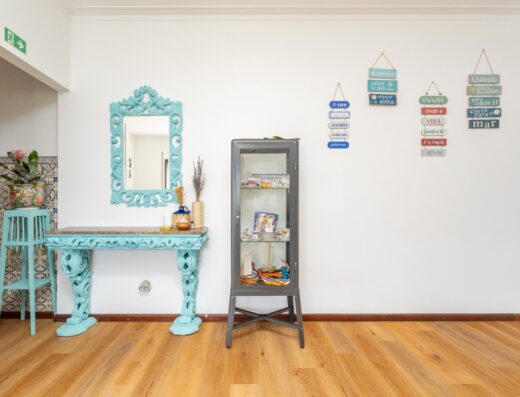 Bright interior with decorative turquoise mirror and console table, coastal-themed wall hangings, and a black display shelf showcasing surf gear and accessories.