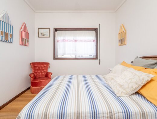 Bright and inviting bedroom at Women Surf Camp in Portugal, featuring a comfortable bed with striped bedding, colorful pillows, and charming wall decor, perfect for relaxing after surfing sessions.