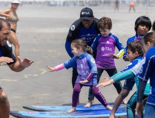 Kids learning to surf with expert instructors on the beach.