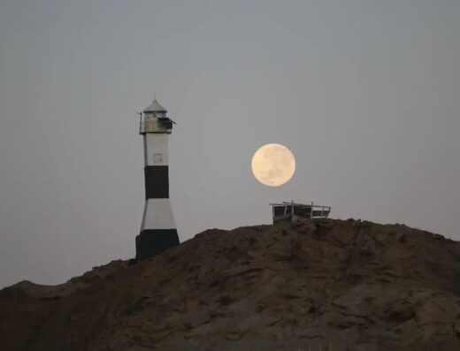 Lighthouse at Casa Faro Cabo Blanco under a full moon, situated on a rocky hilltop with a clear view of the night sky.