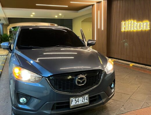 Modern Mazda sedan parked at Hilton hotel entrance in El Salvador, offering premium transportation services for executive travel.