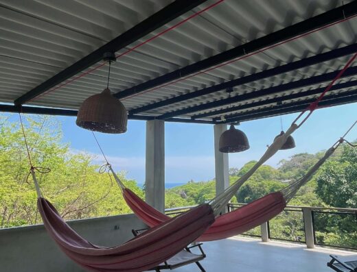 Relaxing hammock on porch overlooking lush greenery and ocean view.