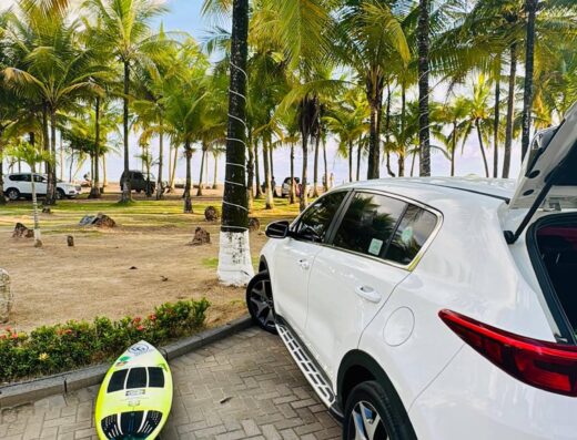 White SUV parked near palm trees with a yellow and black surfboard on the ground, ready for surfing and beach adventures in Costa Rica.