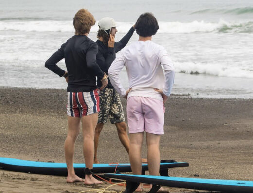 Group of friends preparing surfboards on Jacó beach, Costa Rica, for a surfing session with locals, enjoying the vibrant surf culture and ocean views.