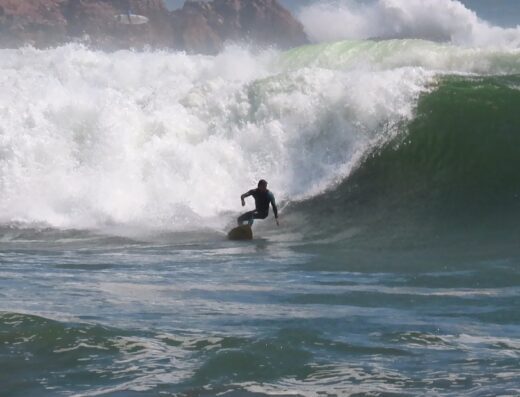 Surfer riding a large wave during an exciting surf adventure at Waverii Beach, showcasing the thrill of ocean surfing and the beauty of the coastal environment.