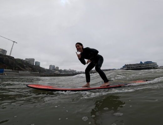 An energetic surfer riding a wave on a paddleboard during a surf adventure, with an urban skyline in the background under cloudy skies.
