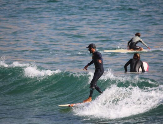 Surfer riding a wave with two other surfers in the background, capturing the essence of surfing and connection with the ocean.