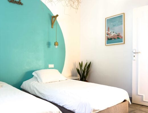 Bright and inviting bedroom with modern decor at La Crique Surf House, featuring comfortable beds, stylish wall art, and natural light, perfect for a relaxing seaside getaway.