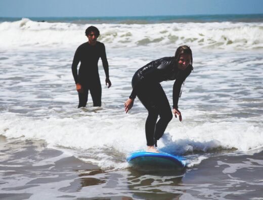Fun surfing session with two people in wetsuits learning on a blue surfboard.