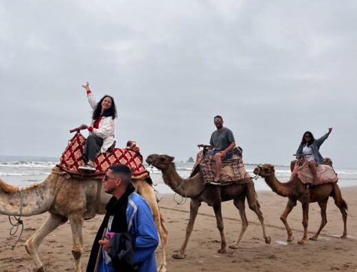 Adventurous camel riding on the beach with friends, showcasing scenic ocean views and fun ambiance during a cloudy day at the seaside resort.