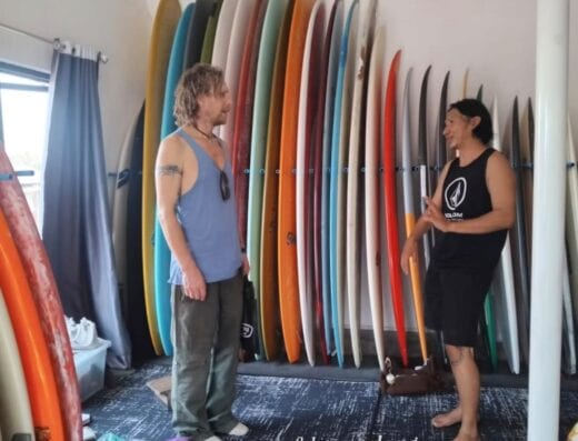 Two men talking inside a surf shop with colorful surfboards on the wall, showcasing surf equipment in Padang.