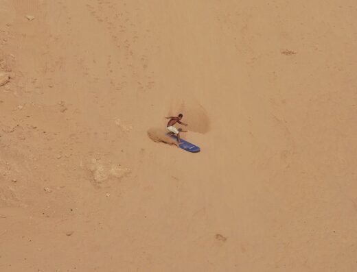 Sandboarding on a steep desert dune with a guide and instructor, highlighting outdoor adventure, sand dunes, and extreme sports activities.