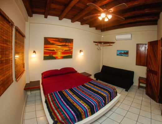 Cozy bedroom with vibrant striped bedspread, wooden ceiling, and ocean-inspired artwork, perfect for relaxing after a day of surfing.