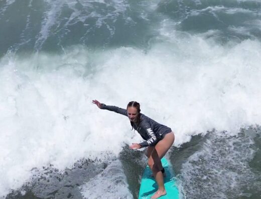 A female surfer riding a wave on a bright turquoise surfboard during a surf class at Waverii.