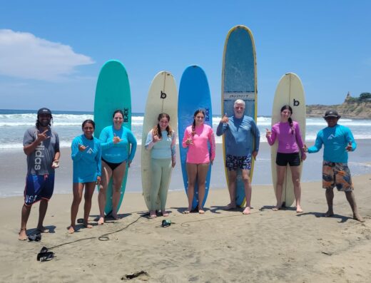 Group of people standing on the beach with surfboards, ready for surf lessons, under a clear blue sky.