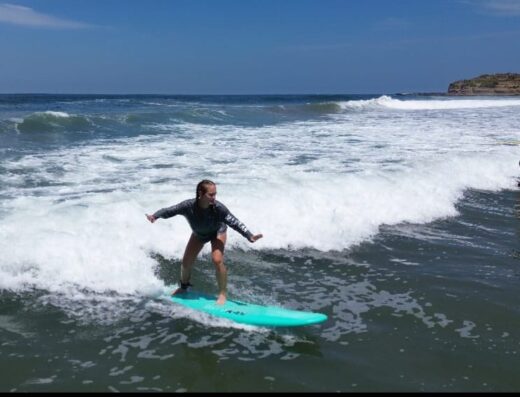 Young girl learning to surf on a wave at Waverii Beach, part of surf classes offered by Waverii for beginners and enthusiasts.