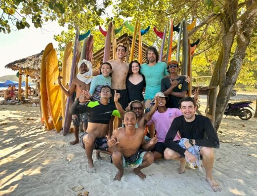 Group of friends enjoying surfing and beach activities at Addict Surf 6 days/7 nights package, with surfboards and tropical beach setting.