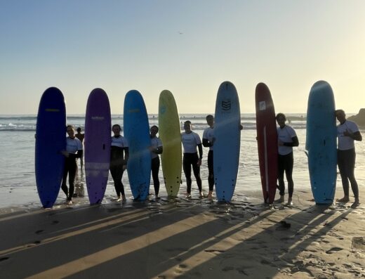 Group of surfers holding colorful surfboards on the beach during sunset, capturing a moment of adventure and relaxation by the ocean.