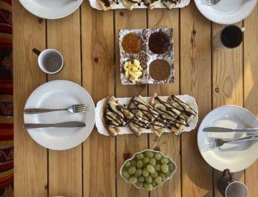 Delicious breakfast with pancakes drizzled with chocolate, fresh fruit, and beverages, perfect for fueling a surf and yoga adventure.